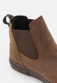 Bottine Chelsea marron en cuir avec panneau latéral élastique, languette d'extraction et doublure intérieure noire rembourrée.