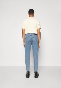 Světležluté tričko s krátkými rukávy spárované s světle modrými džíny. Džíny mají úzký střih a dvě zadní kapsy. Černá obuv s akcenty.