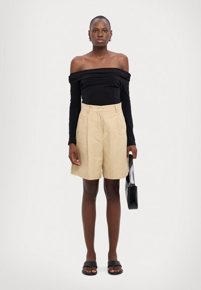 Schwarzes, schulterfreies Oberteil mit langen Ärmeln, beigefarbene, hoch geschnittene Shorts, schwarze Rutschen-Sandalen und eine kleine schwarze Handtasche. Glatte Texturen und neutrale Farbtöne.