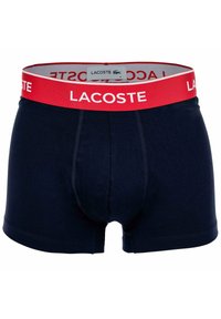 Boxer in cotone per uomo di colore blu navy con una ampia cintura rossa che presenta il marchio "LACOSTE" in bianco e una piccola etichetta con il logo Lacoste.