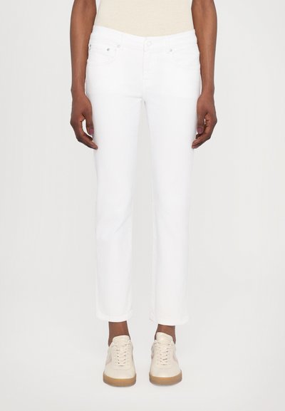 Jean en denim blanc avec une coupe droite, style à cinq poches et fermeture à bouton. Portés avec des baskets beiges.