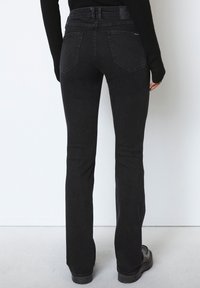 Jean flare noir avec une texture lisse, comportant des poches arrière et une taille haute. Le design met en avant un look ajusté au niveau des cuisses.