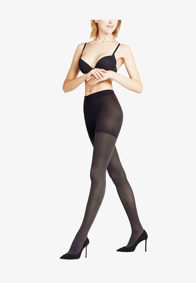 Sorte uigennemsigtige strømpebukser med en glat tekstur, der har en høj talje og en overgang til en gennemsigtig top. Sammen med sorte højhælede sko.