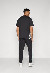 Tricou negru din bumbac cu mâneci scurte și dungi albe pe laterale, asortat cu pantaloni jogger negri care au dungi de accent teal și adidași albi.