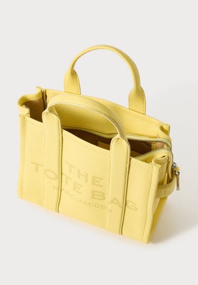 Gelbe Leder-Tote mit Griffen oben, Reißverschlussverschluss und prägnierter Schrift. Verfügt über eine strukturierte Oberfläche und ein kontrastierendes Innenfutter.
