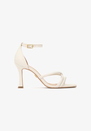 Baltas odinis sandalai su plonu kulkšnies dirželiu, auksine sagtimi ir susikertančiomis juostelėmis priekyje. Turi siaurėjantį stileto kulną.