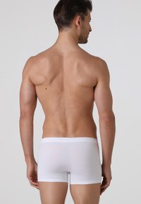 Boxer briefs bianchi in cotone con una vestibilità aderente, elastico in vita e una texture liscia, mostrati da dietro su un modello con capelli corti.
