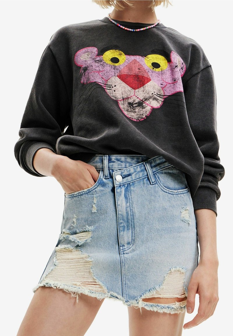 Personne portant un sweat-shirt noir avec un grand imprimé visage de la panthère rose et une mini-jupe en denim déchiré bleu clair à taille haute.