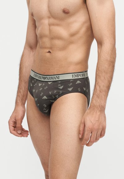 Άνδρας με τονωμένο κορμό που φοράει σκούρα σλιπ με ανοιχτό γκρι ζώνη μέσης με το λογότυπο "Emporio Armani" και μοτίβα.