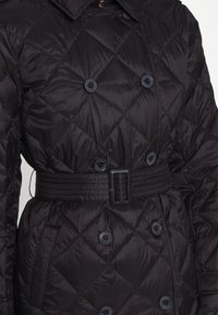 Svart quiltad vadderad jacka med skärp i midjan, med dubbelknäppt knäppning och diamantmönstrad textur.