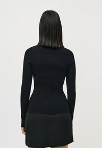Pulover negru din tricot fixat, cu mâneci lungi, ajustat pe corp și cu o textură netedă. Purtați cu o fustă neagră, văzut din spate.