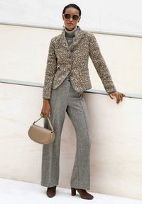 Patroon wol blazer met ronde kraag en knoopsluiting, gecombineerd met grijze wijde broekspijpen. Witte en beige handtas, bruine sleehakken.
