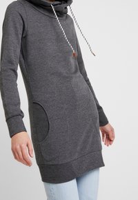 Szara sukienka-dres z kapturem, długimi rękawami i przednią kieszenią. Posiada żebrowany dół oraz sznurek ściągający z drewnianymi akcentami.