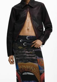 Bordoopunane nahktagi kontrastsete õmblustega, mida on kombineeritud mitmevärvilise trükitud seelikuga, millel on julged graafilised mustrid ja pandlaga vöökohat detail.