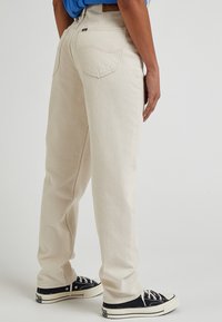 Krémové denimové džíny s rovnými nohavicemi, obsahující zadní kapsy a jemné prošívání, doplněné černými teniskami.