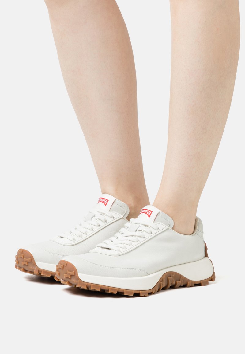 White leather sneakers with lace-up design, rubber outsole, and brown traction pattern; red branding on tongue.