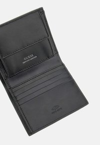 Ce portefeuille en cuir noir dispose de plusieurs emplacements pour cartes et d'une texture lisse. "GUESS CUIR AUTHENTIQUE" est embossé à l'intérieur. Logo de protection RFID inclus.