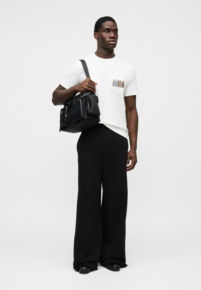 Λευκό μπλουζάκι με πολύχρωμο σχέδιο στην τσέπη, συνδυασμένο με φαρδιά μαύρη παντελόνια. Μαύρη τσάντα με υφή και ιμάντα ώμου.