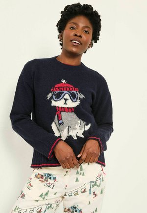 Marineblaues Sweatshirt mit einem gestrickten Hundedesign, das einen roten und grauen Hund in Ski-Bekleidung zeigt. Rüschensaum und -manschetten mit roten Akzenten. Schlafanzughose mit Ski-Motiven.