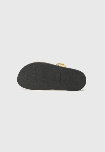 Des chaussures avec une semelle en caoutchouc noir texturé, un matériau supérieur de couleur claire et deux sangles ajustables.
