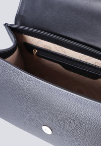 Borsa in pelle nera con texture, dotata di una tasca con zip e rivestimento interno beige con stampa logo discreta, hardware argentato e chiusura a scatto circolare.