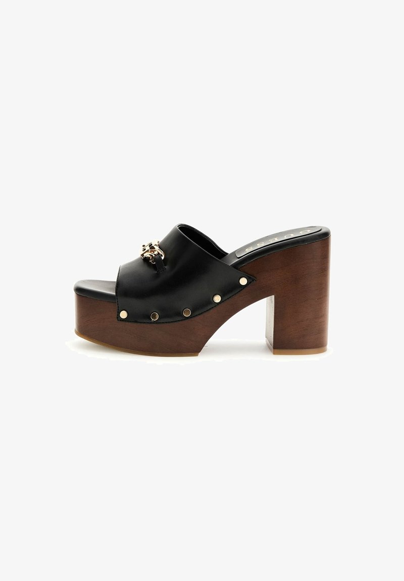 Mule en cuir noir avec détail de chaîne dorée, semelle plateforme en bois et talon carré sur fond blanc.