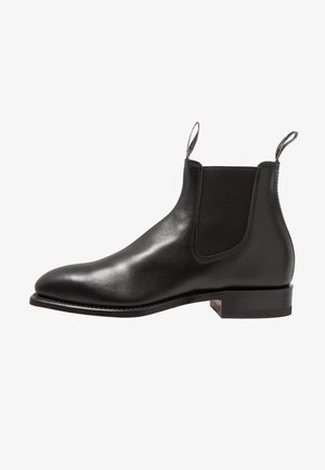 Black leather Chelsea boot with elastic side panels, rounded toe, and pull tabs; features a stacked wooden heel and smooth texture.