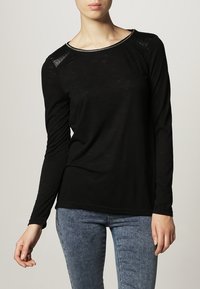 Czarna bluzka z długim rękawem, okrągłym dekoltem, teksturowanymi detalami na ramionach oraz luźnym krojem. Tkanina wydaje się lekka i lekko przezroczysta.