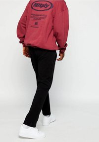 Bordowa bluza z nadrukiem oraz czarne spodnie, uzupełnione białymi trampkami. Bluza ma luźny krój i opuszczone ramiona.