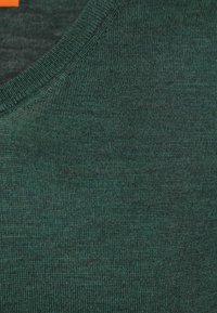 Donkergroen gebreide stof met een gladde textuur, voorzien van een fijn geribde ronde halslijn. Subtiele kleurvariaties doorlopend.