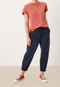 Camiseta de manga corta a rayas rojas y blancas combinada con pantalones cargo azul marino. El calzado consiste en zapatillas de lona rojas con suelas y cordones blancos.