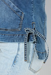 Džínová bunda s postranním vázáním, charakteristická tmavě modrým praním, kontrastním prošíváním a postranní kapsou na světle modrých džínách.