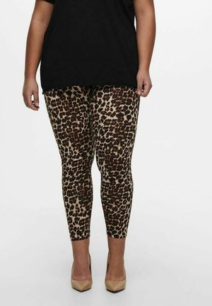 Leopard print leggings in tan and black, featuring a fitted design. Worn with a loose black top and nude heels. Smooth texture and stretchy fabric.