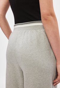 Szare dresy wykonane z miękkiego materiału mają szeroką elastyczną talię z czarno-białymi paskami. Pokazane z tyłu, z widocznymi detalami kieszeni.