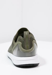 Grön nätverksko med transparenta detaljer och en strukturerad hälkappa. Utrustad med en dragflik och vit mellansula med en svart gummisula.