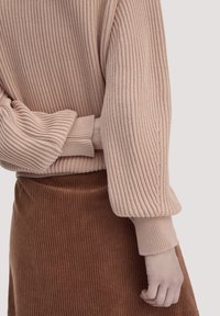 Strickpullover in zartem Pink mit gerippter Textur, mit breiten, leicht gepufften Ärmeln und einem passenden, gerippten Bündchen, kombiniert mit einem braunen Baumwollrock.