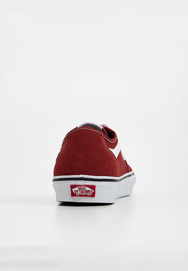 Zapatilla baja de ante rojo con franjas laterales blancas, suela de goma y logo de Vans en la parte trasera. Diseño limpio con ribetes negros.