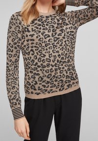 Pull en imprimé léopard dans des tons de beige et noir, fabriqué en un matériau tricoté doux. Il présente des poignets côtelés rayés et un col rond.