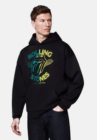 Czarna bluza z kapturem wykonana z bawełny, z graficznym nadrukiem z przodu przedstawiającym logo Rolling Stones, wyraźnym tekstem i kolorowymi akcentami. Posiada kieszeń typu kangur.