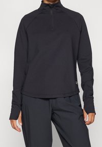 Schwarzes Langarm-Pullover mit einem halben Reißverschluss am Kragen. Hergestellt aus glattem, leichtem Material. Verfügt über Raglanärmel und dezente Branding am Saum.