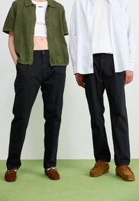 Green knit button-up shirt, white cropped top, black trousers, and brown suede shoes on two figures against a light background with green floor.