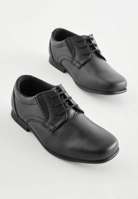 Chaussures en cuir noir avec un bout rond, un laçage, et des détails de couture subtils. Semelle plate et texture lisse.