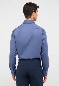 Camicia a maniche lunghe in morbido tessuto blu, con colletto classico e polsini abbottonati. Tessuto liscio con vestibilità sartoriale, vista posteriore in esposizione.