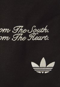 Svart stoff med hvit brodert tekst: "Fra Sør. Fra Hjertet." og en hvit Adidas trefoil-logo med tre striper.