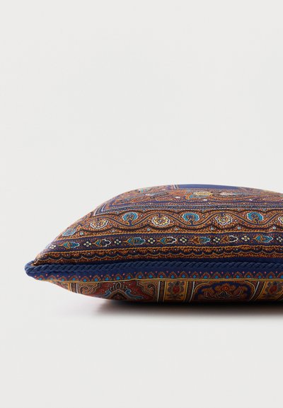 Coussin décoratif rectangulaire avec motifs complexes de paisley et floraux en tons bleus, bruns et dorés sur un fond blanc.