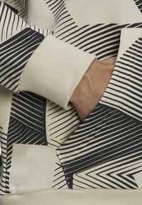 Main dans une poche en tissu crème avec un motif géométrique rayé noir et blanc et un bord-côte côtelé.