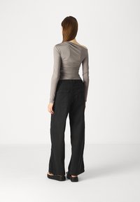 Long-sleeve, off-shoulder top in light gray, paired with loose-fitting black pants featuring buttoned back pockets. Black slip-on shoes.