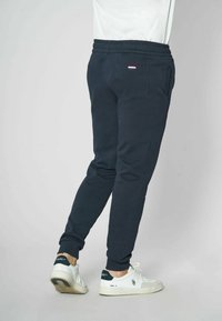 Pantaloni della tuta color navy con vita elasticizzata, design a gamba affusolata, tasche laterali e una piccola etichetta con marchio sulla tasca posteriore.