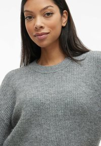 Sivkasta pletenega puloverja s krožnim izrezom, ki ima teksturiran rebrast vzorec. Mehak material in udoben kroj z dolgimi rokavi.