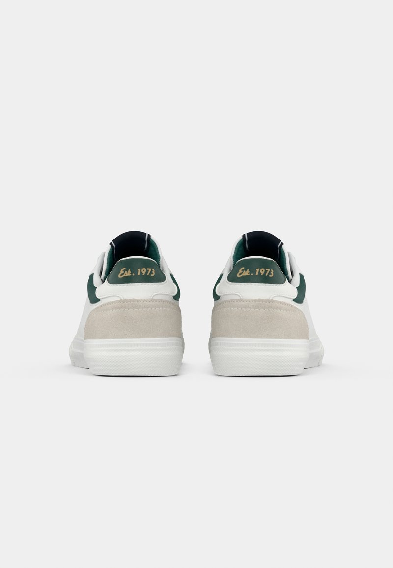 Witte sneakers met groene accenten, een suède hiel en contrasterende texturen. Kenmerkt retro branding "Est. 1973" op de achterkant.
